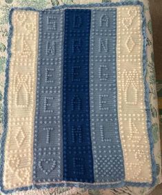 a blue and white crocheted blanket sitting on top of a couch next to a pillow