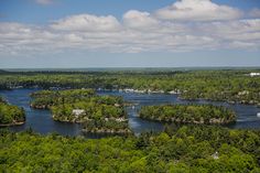 an aerial view of a lake surrounded by trees and houses in the distance with clouds overhead