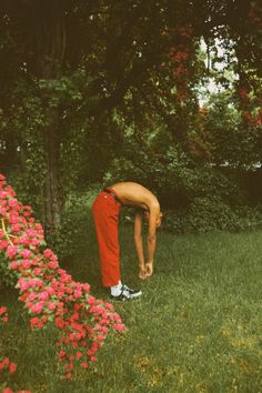 a man bending over in the grass next to flowers