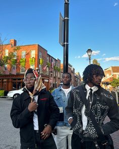 three young men standing next to each other on the side of a street with buildings in the background