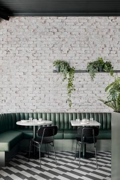 a restaurant with white brick walls and green velvet boothes, black chairs and potted plants on the wall