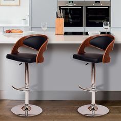 two black and chrome bar stools in front of a kitchen counter with wine glasses on it