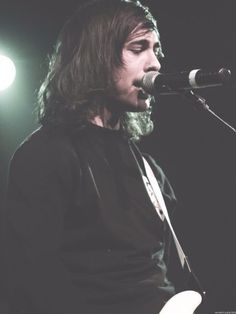 a man with long hair playing a guitar in front of a microphone and some lights