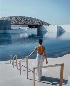 a woman in a white dress is walking down the stairs to an outdoor swimming pool