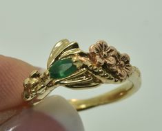 a close up of a person's hand holding a gold ring with an emerald stone