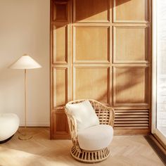 a white chair sitting next to a lamp on top of a hard wood floor in front of a wooden paneled wall