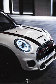 the front end of a white and black mini cooper parked in a parking lot at night