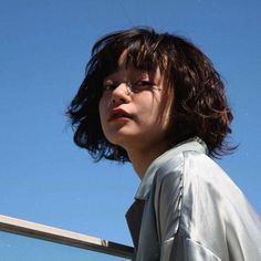 a woman with dark hair standing next to a fence and looking off into the distance