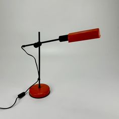 an orange table lamp with a black cord attached to the base and a red light plugged into it