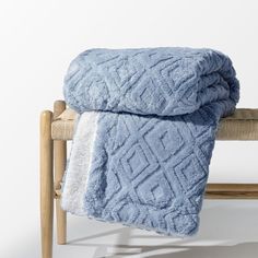 two blue blankets sitting on top of a wooden bench next to a white wall and chair