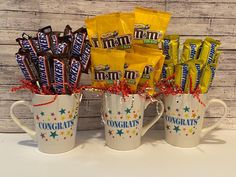 three coffee mugs filled with candy bars and wrapped in red, white and blue ribbon