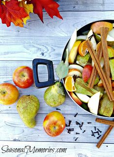 apples, oranges and cinnamon sticks are arranged in a bowl on a white wooden table