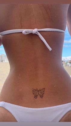 a woman with a butterfly tattoo on her lower back, standing in front of the ocean