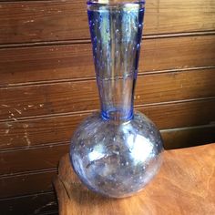 a blue glass vase sitting on top of a wooden table next to a wood paneled wall