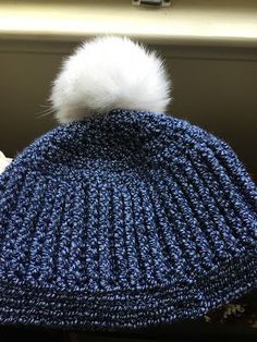 a blue knitted hat with a white pom - pom sitting on top of it