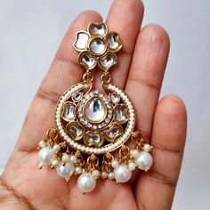 Adorn yourself in timeless splendor with our Beautiful Golden Chandbali Earrings embellished with Kundan and Zircon Stones, featuring suspended white pearl hangings. These earrings are a masterpiece of elegance, seamlessly blending traditional charm with contemporary design. The golden chandbali shape exudes regal allure, while the intricate detailing of Kundan and Zircon stones adds a touch of opulence. The ethereal white pearls suspended from the earrings create a graceful movement, making them a perfect choice for special occasions. Elevate your style with these exquisite earrings that embody sophistication and capture the essence of classic beauty. Materials: Brass, Pearl, Kundan & Zircon Stone ❋❋ Shipping Methods ❋❋ Standard Delivery - Take up to 8-14 business days (Worldwide). ❋❋ Ple White Hand Set Chandelier Earrings For Celebrations, White Bridal Earrings With Stone Work For Celebration, White Round Chandbalis For Celebrations, White Bridal Earrings For Festivals And Anniversary, White Bridal Earrings For Festivals And Anniversaries, Fusion Style Bridal Earrings With Intricate Design In White, White Hand Set Chandbalis For Diwali, Hand Set White Fusion Bridal Earrings, White Round Chandbalis For Diwali