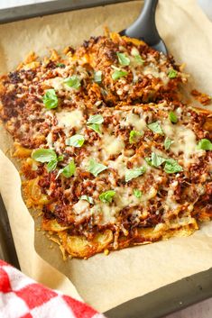 two pizzas with cheese, meat and herbs are on a baking sheet next to a red checkered table cloth