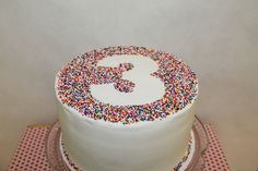 a white cake with sprinkles and the number three on it