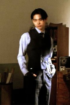 a young man is standing in front of a bookcase and looking at the camera