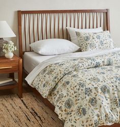 a bed with white sheets and blue flowers on the comforter is next to a night stand