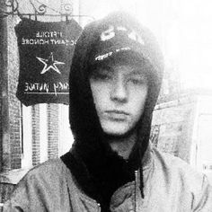 black and white photograph of a man wearing a hoodie in front of a sign