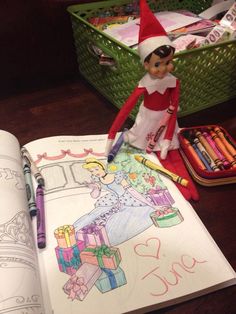 an elf is sitting on top of a book with crayons and markers in front of it