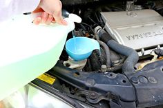 a person is cleaning the engine of a car with a blue cup and spray bottle