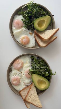 two bowls filled with eggs, bread and greens on top of a white countertop