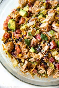 a glass bowl filled with chicken, avocado, and black beans salad on top of a white table