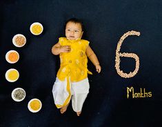 a baby laying in front of the number six on a black surface next to bowls and grains