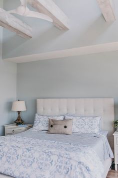 a bedroom with blue and white bedding, two nightstands and a ceiling fan