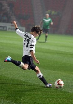 a young man kicking a soccer ball on a field with other players in the background