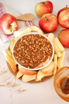 an apple and peanut butter dip surrounded by apples, crackers, and caramel