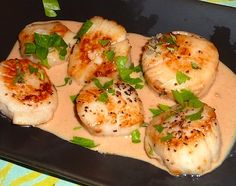 some scallops are sitting on a black plate with sauce and garnish