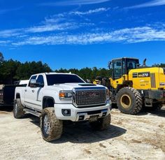 two large trucks parked next to each other on a dirt field with trees in the background