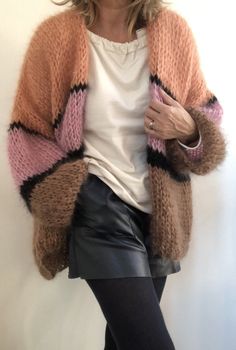 a woman is posing in front of a white wall wearing a pink and black cardigan