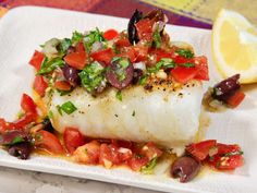 a fish dish with tomatoes, olives, and other vegetables on a white plate