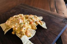 a tortilla chip topped with cheese and other toppings on a wooden tray