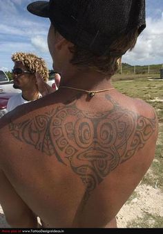 a man with a tattoo on his back standing in front of a car and another man behind him