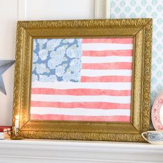 an american flag is displayed in a gold frame on a mantel with other decorations