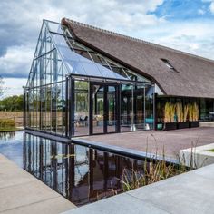 a glass house with a pond in front of it and a thatched roof on top