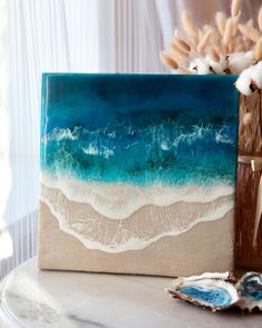 an ocean scene painted on a canvas next to seashells