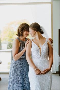 two women standing next to each other in front of a window wearing wedding gowns