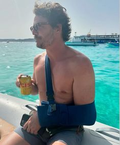 a shirtless man sitting on a boat with a can of beer in his hand