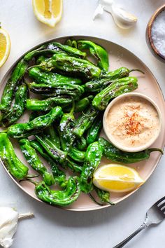 a plate filled with green peppers next to lemon wedges and garlic on a white table