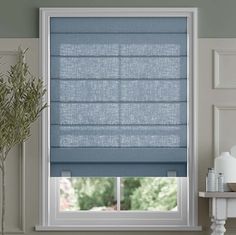 a window with blue roman shades in a living room next to a white table and chair