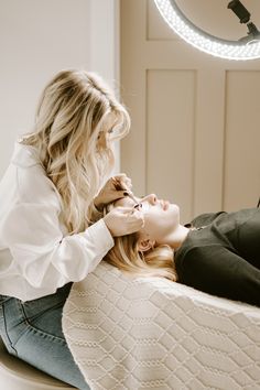 a woman is getting her hair styled by another woman in the mirror while sitting on a bed