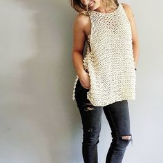 a woman standing in front of a wall wearing ripped jeans and a crochet top