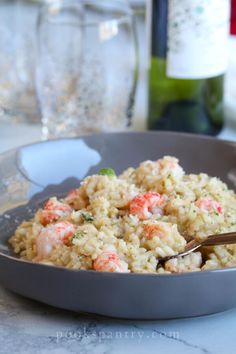 a bowl filled with rice and shrimp on top of a table next to wine bottles