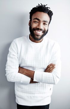 a smiling man with his arms crossed in front of him, wearing a white sweater and black pants